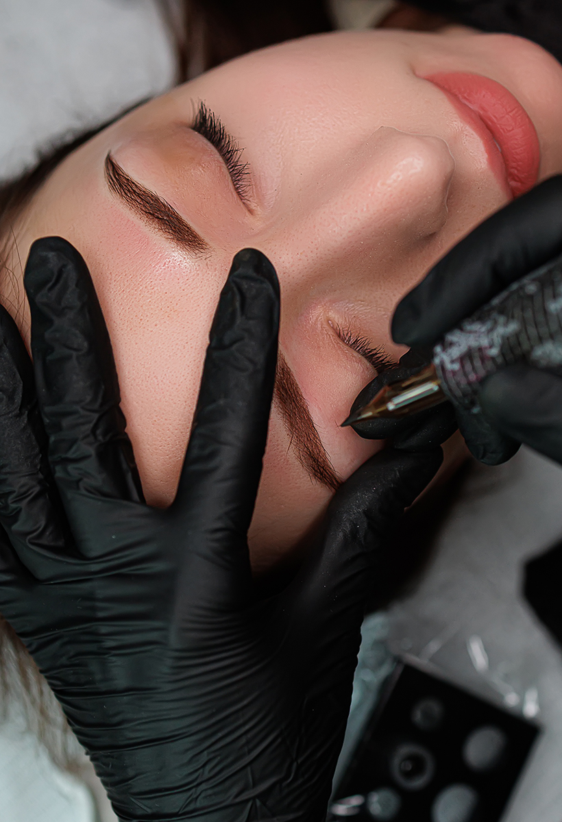 The master holds the model's eyebrows with his fingers and applies the eyebrow permanent. Eyebrow permanent makeup cosmetic procedure.